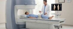 Paciente sorridente a realizar exame de ressonância magnética aberta num equipamento Hitachi AIRIS Elite da REMA Aberta em Alverca, com foco numa lesão no joelho.