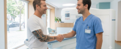 Paciente com tatuagem no braço conversa com profissional de saúde antes de fazer ressonância magnética aberta.